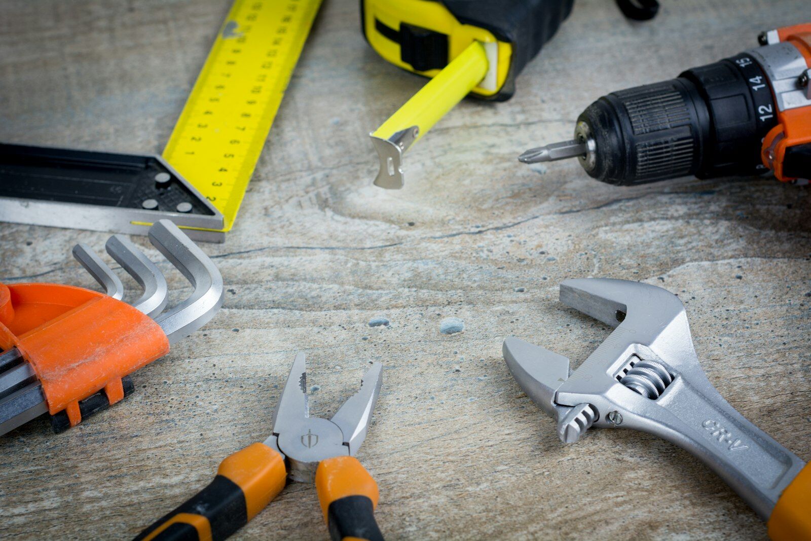 Tape measure, adjustable wrench, pliers and drill on a wood surface